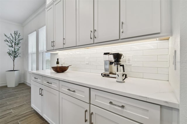 bar featuring tasteful backsplash, white cabinetry, light stone countertops, and crown molding