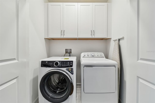 clothes washing area with separate washer and dryer and cabinets