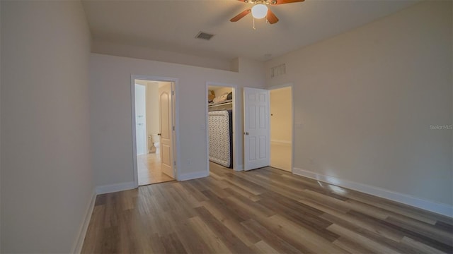 unfurnished bedroom with a spacious closet, ceiling fan, a closet, and hardwood / wood-style floors