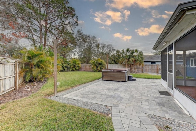 patio terrace at dusk featuring a hot tub, a yard, and a sunroom