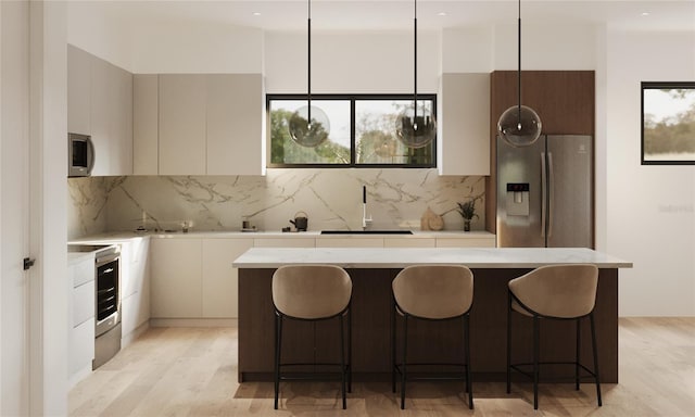 kitchen featuring a sink, light countertops, appliances with stainless steel finishes, modern cabinets, and a kitchen bar