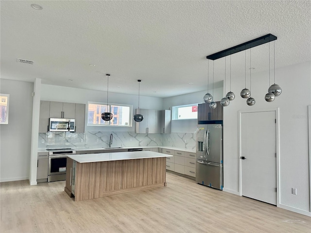 kitchen featuring appliances with stainless steel finishes, backsplash, a kitchen island, and gray cabinetry