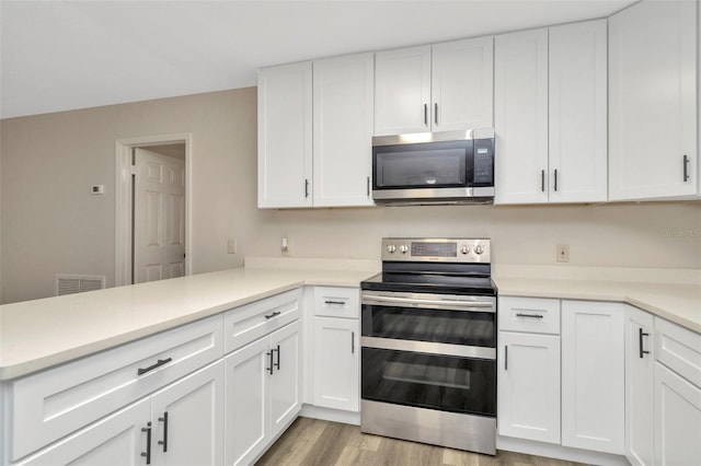 kitchen with appliances with stainless steel finishes, kitchen peninsula, light hardwood / wood-style floors, and white cabinets