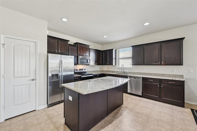 kitchen with dark brown cabinetry, sink, light stone counters, a center island, and appliances with stainless steel finishes