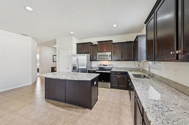 kitchen featuring dark brown cabinetry, sink, a center island, appliances with stainless steel finishes, and light stone countertops