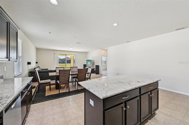 kitchen with dishwasher, a center island, light stone counters, dark brown cabinetry, and a textured ceiling