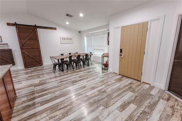 dining room with a barn door, lofted ceiling, and light hardwood / wood-style flooring