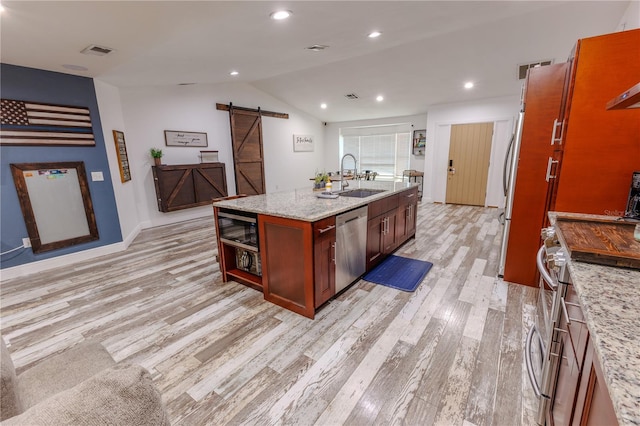 kitchen featuring sink, appliances with stainless steel finishes, light stone counters, an island with sink, and a barn door