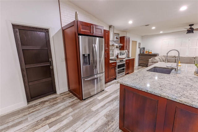 kitchen featuring wall chimney exhaust hood, sink, light stone counters, light hardwood / wood-style flooring, and stainless steel appliances