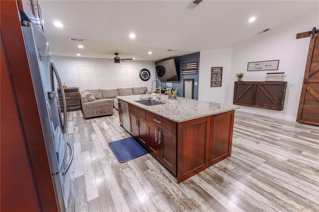 kitchen featuring sink, a center island with sink, light wood-type flooring, a barn door, and light stone countertops