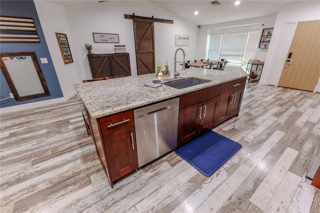 kitchen with sink, dishwasher, light stone countertops, an island with sink, and a barn door