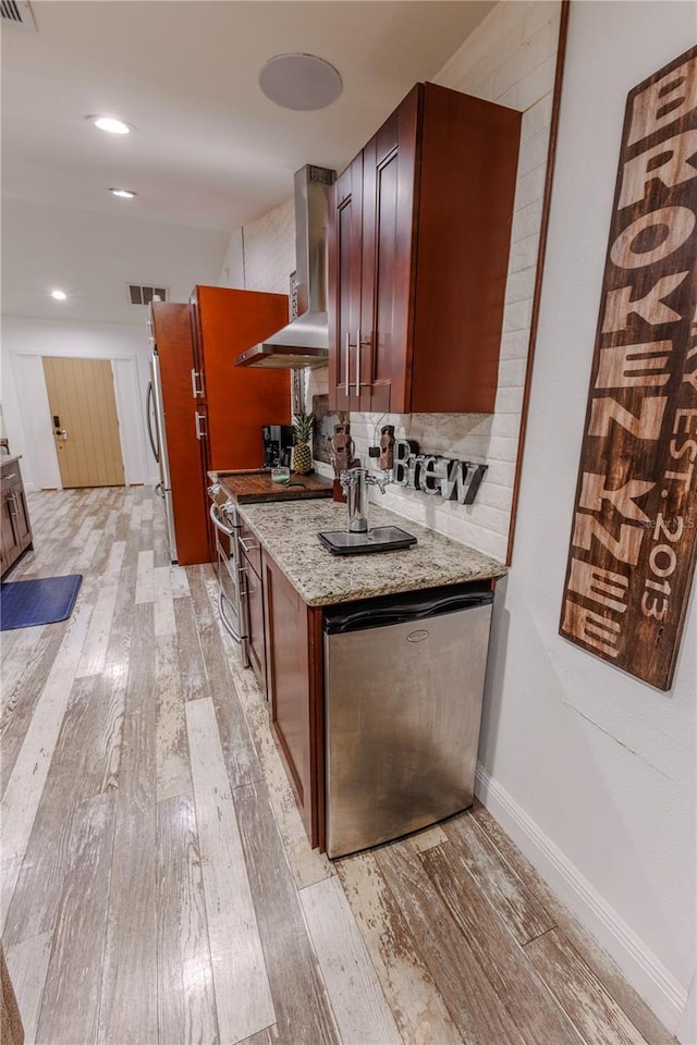 kitchen with stainless steel stove, dishwasher, wall chimney exhaust hood, light stone counters, and light hardwood / wood-style flooring