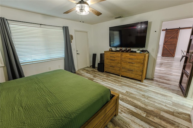 bedroom with a barn door, ceiling fan, and light wood-type flooring