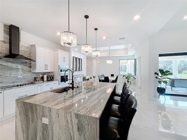 kitchen with black electric cooktop, a spacious island, wall chimney range hood, pendant lighting, and white cabinets