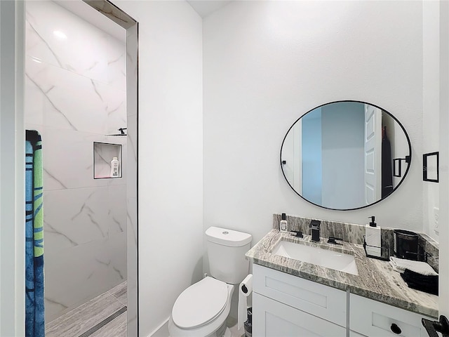 bathroom with toilet, vanity, and tiled shower