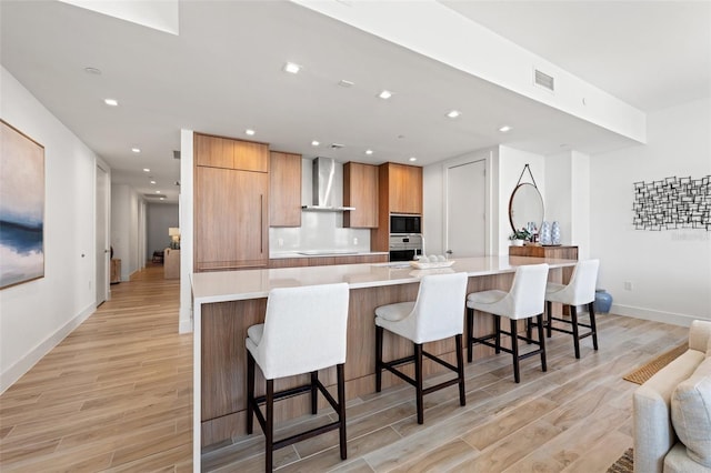 kitchen featuring a large island, wall chimney range hood, a breakfast bar, black appliances, and light hardwood / wood-style floors