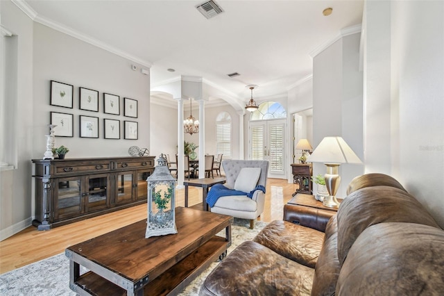 living room with crown molding, ornate columns, a chandelier, and light wood-type flooring