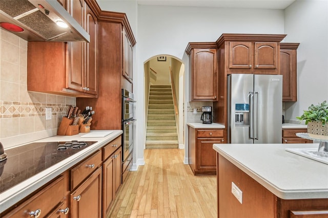 kitchen featuring ventilation hood, stainless steel appliances, light hardwood / wood-style flooring, and backsplash