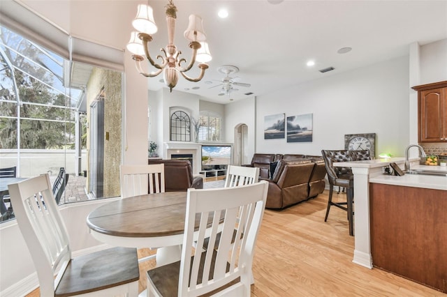 dining space featuring sink, ceiling fan with notable chandelier, and light hardwood / wood-style flooring