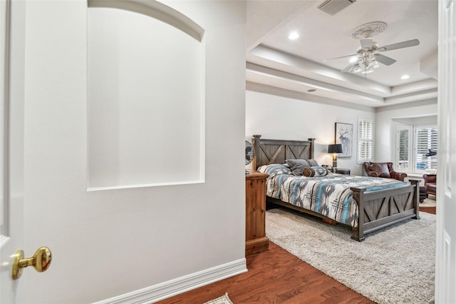 bedroom featuring ceiling fan, dark wood-type flooring, and a tray ceiling