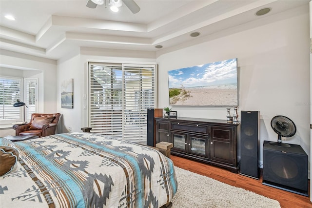 bedroom with ceiling fan, wood-type flooring, and a tray ceiling