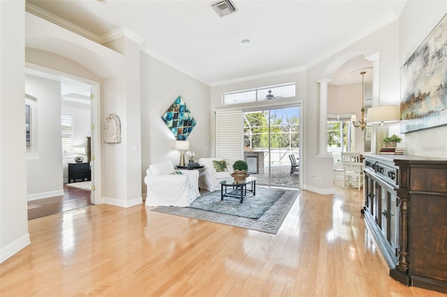 living area with visible vents, ornamental molding, light wood-style floors, baseboards, and a chandelier