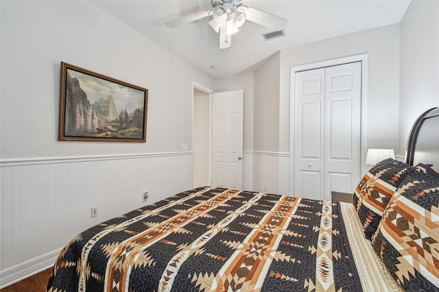 bedroom with visible vents, a wainscoted wall, a ceiling fan, wood finished floors, and a closet