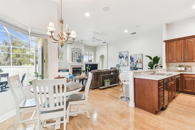 kitchen featuring a kitchen bar, light wood-style flooring, a peninsula, a glass covered fireplace, and a sink