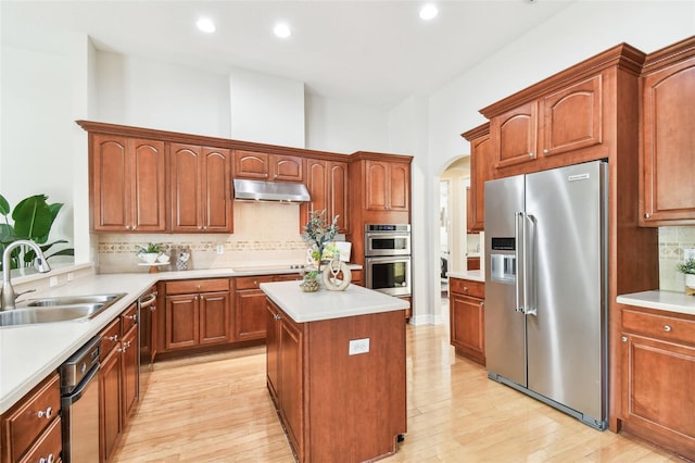 kitchen featuring a kitchen island, arched walkways, a sink, stainless steel appliances, and under cabinet range hood