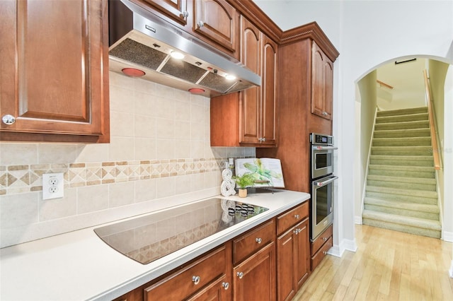 kitchen featuring black electric stovetop, under cabinet range hood, double oven, light countertops, and decorative backsplash