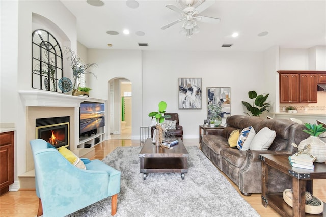 living room featuring arched walkways, visible vents, light wood-style flooring, and a glass covered fireplace