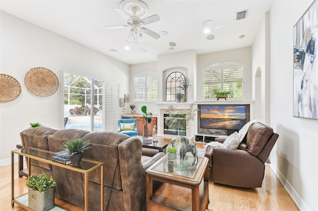 living area featuring visible vents, baseboards, a fireplace, ceiling fan, and light wood-style floors