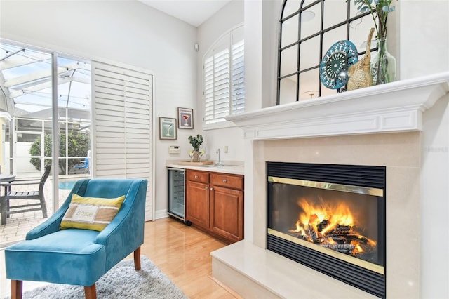 sitting room featuring beverage cooler, a glass covered fireplace, indoor wet bar, and light wood-type flooring