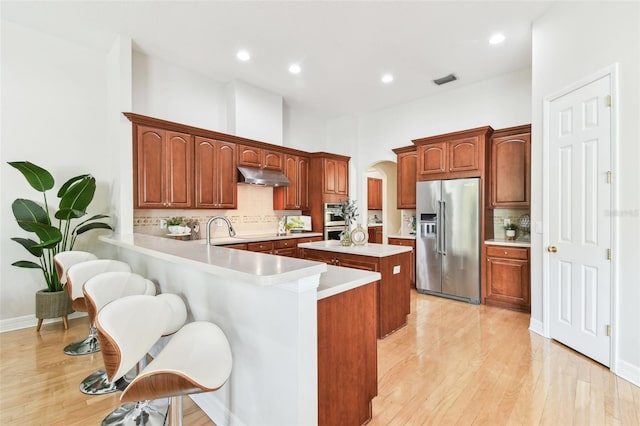 kitchen with arched walkways, light countertops, under cabinet range hood, appliances with stainless steel finishes, and a center island