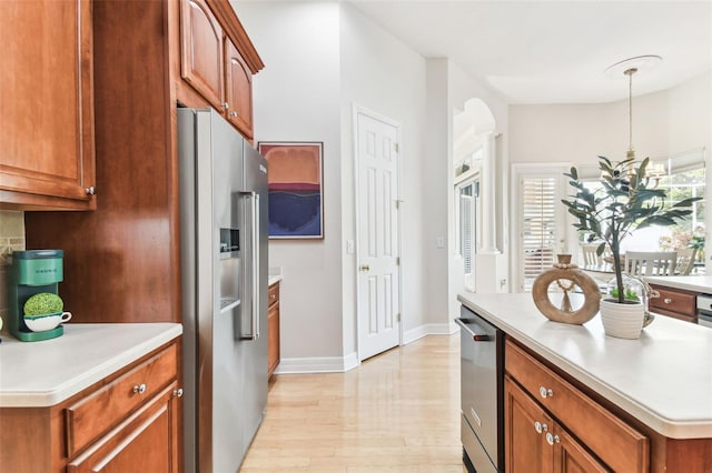 kitchen with brown cabinetry, light wood-style flooring, light countertops, appliances with stainless steel finishes, and decorative light fixtures