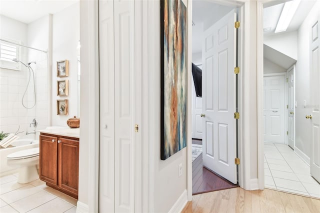 full bath featuring baseboards, toilet, vanity, wood finished floors, and washtub / shower combination