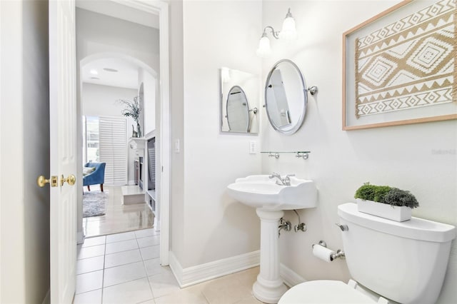 bathroom with tile patterned floors, toilet, a fireplace, and baseboards