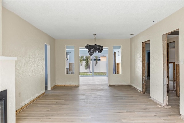 unfurnished dining area with a textured ceiling, light hardwood / wood-style floors, and a notable chandelier