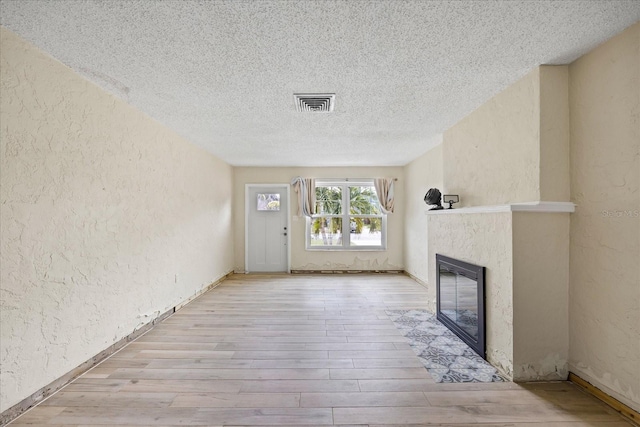 unfurnished living room with a high end fireplace, a textured ceiling, and light hardwood / wood-style floors