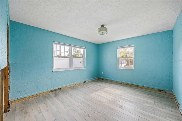 empty room featuring light hardwood / wood-style floors, a textured ceiling, and a healthy amount of sunlight