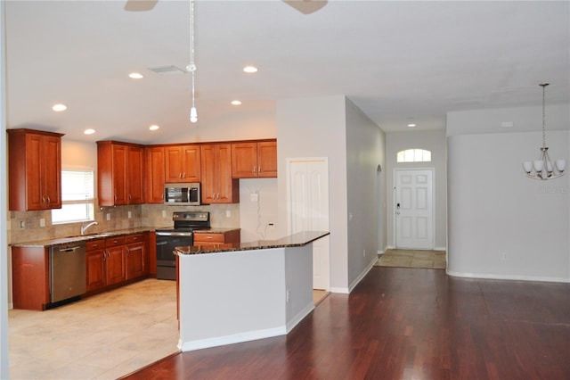 kitchen featuring stainless steel appliances, a center island, dark stone counters, pendant lighting, and sink