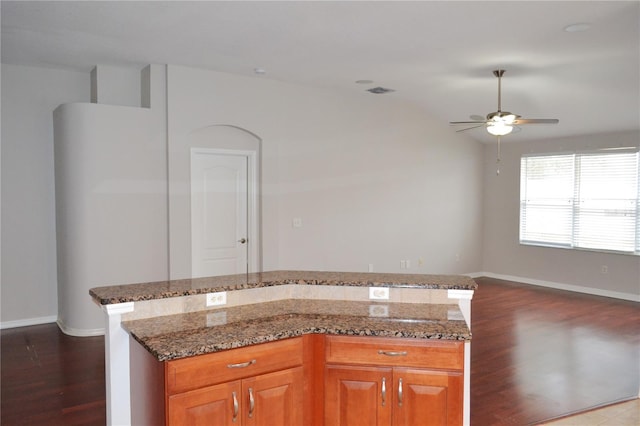 kitchen featuring ceiling fan, dark wood-type flooring, a center island, and dark stone counters