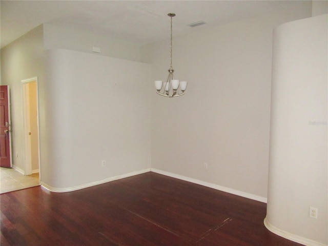 empty room featuring wood-type flooring and a chandelier