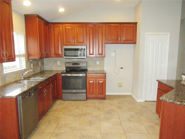 kitchen featuring appliances with stainless steel finishes, light tile patterned flooring, lofted ceiling, dark stone counters, and sink