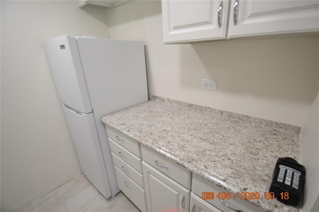 kitchen featuring light tile patterned flooring, white refrigerator, white cabinets, and light stone counters