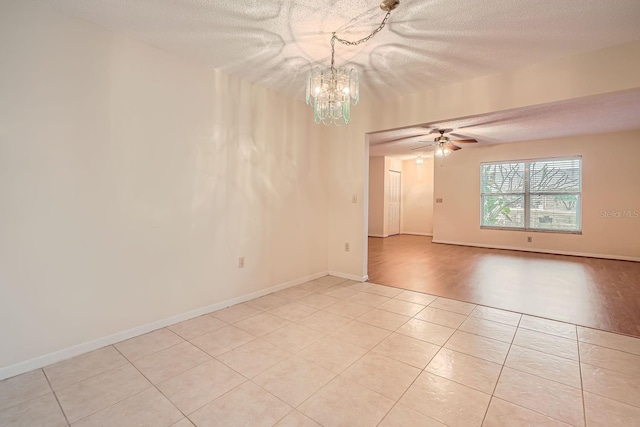 tiled spare room with ceiling fan with notable chandelier and a textured ceiling