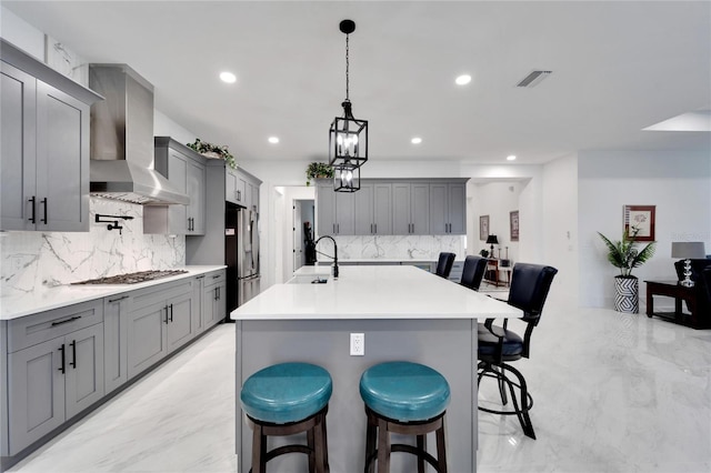 kitchen featuring a breakfast bar, wall chimney range hood, and gray cabinets