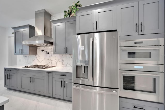 kitchen with backsplash, gray cabinetry, stainless steel appliances, and wall chimney exhaust hood