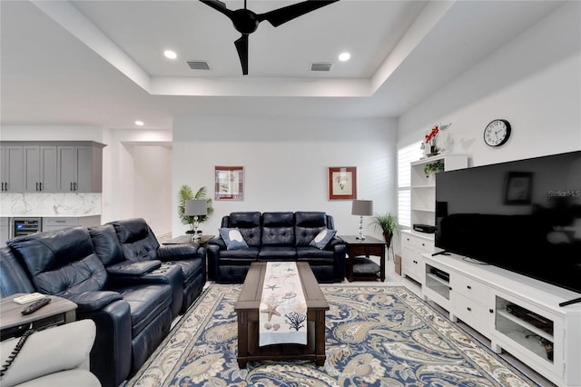 living room with a tray ceiling, beverage cooler, and ceiling fan