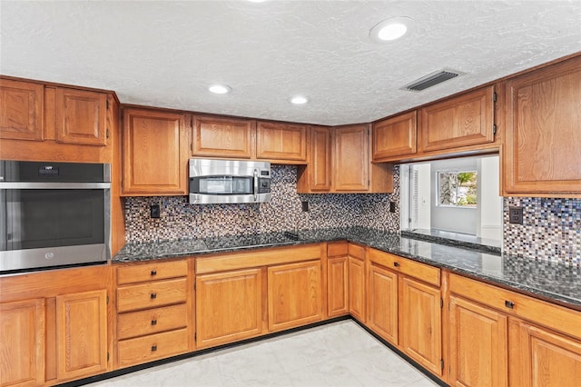 kitchen featuring backsplash, stainless steel appliances, light tile patterned floors, and dark stone countertops